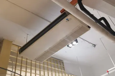Unité intérieure de pompe à chaleur air-air fixée sous une dalle de béton, gaine et câbles apparents