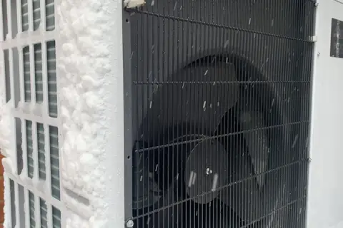 Unité extérieure de pompe à chaleur pendant une chute de neige, grille et hélice couvertes de flocons